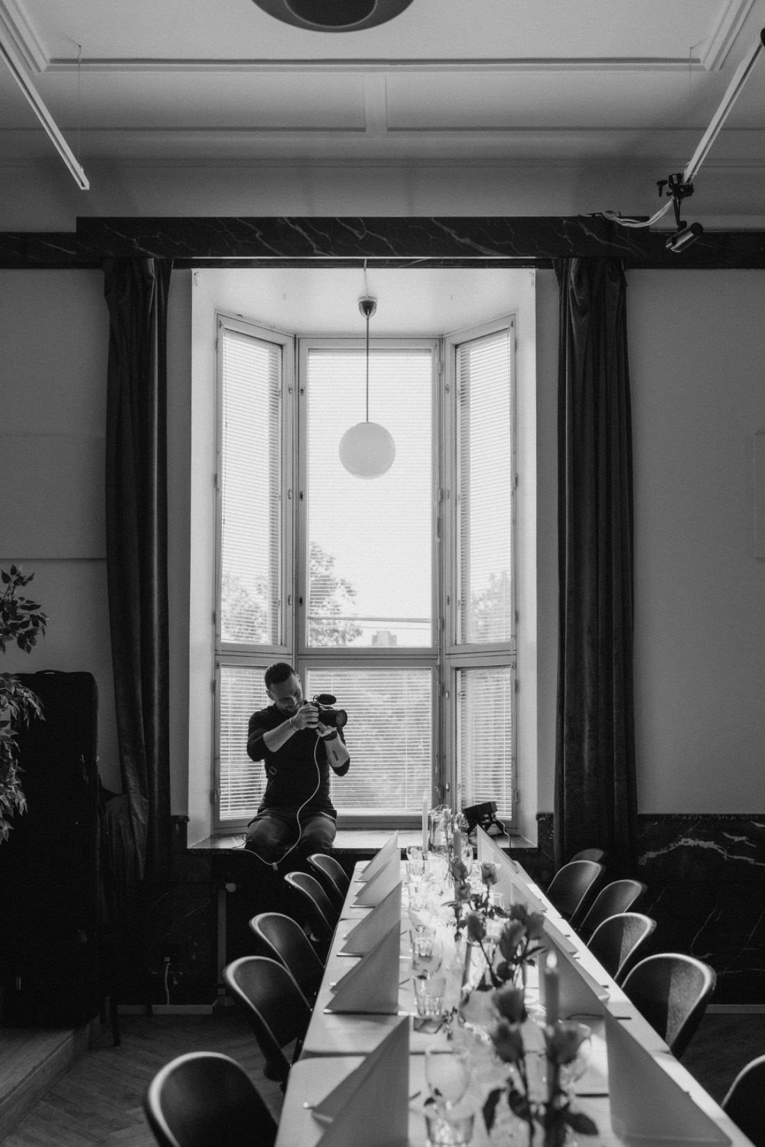 Bastian sitting on a windowsill filming over a candlelit wedding table